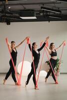 Girls in black are doing fitness with red ribbons indoors photo