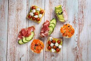 An assortment of sandwiches with fish, cheese, meat and vegetables lay on the wooden table photo