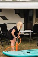 A woman inflates a sup-board for swimming near her motorhome photo