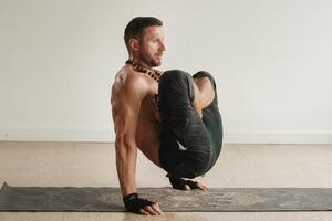 a man with a naked torso does yoga standing on his hands indoors. Fitness Trainer photo