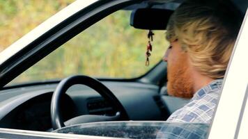 une ivre homme avec une Jaune barbe est assis dans un vieux voiture video