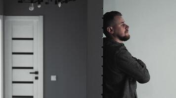 solitario hombre en el habitación, un contemplativo hombre soportes con brazos cruzado en un minimalista habitación, perdido en pensamiento. video