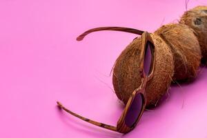 three whole coconuts and wooden glasses on a pink background photo