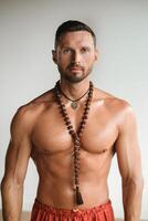 A muscular man with a bare torso and an amulet is standing in the room photo