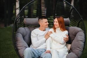 un contento familia es sentado en un hamaca en el césped cerca el casa foto