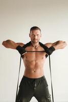 A man with a naked torso is engaged in strength fitness using a rubber loop indoors photo
