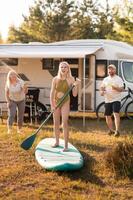 the family is resting next to their mobile home. My daughter is standing with a paddle on a sup board, and her parents pour water on her photo
