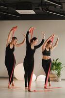 Girls in black are doing fitness with red ribbons indoors photo