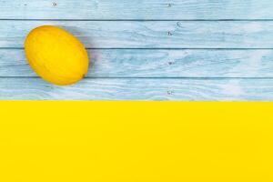 A whole yellow melon lies on a blue wooden background and a yellow background photo