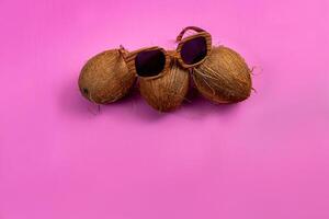 three whole coconuts and wooden glasses on a pink background photo