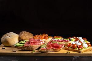 An assortment of sandwiches with fish, cheese, meat and vegetables lay on the board and a bun photo