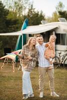 Happy parents with their child play with a kite near their motorhome in the forest photo