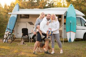 Happy parents with their child playing with a ball near their mobile home in the woods photo