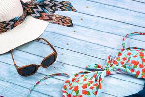 Top view of a straw white hat with glasses and a swimsuit, lying on a blue wooden background.Summer vacation concept photo