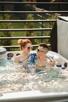 In summer, a man and a woman with glasses of wine relax in the outdoor hot tub photo