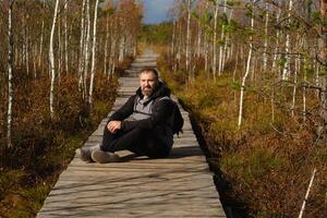 un hombre se sienta en un de madera camino en un pantano en yelnya, bielorrusia foto