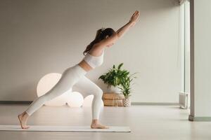 A girl in white clothes does yoga on a mat indoors photo