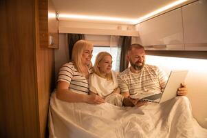 A family of three is watching a movie on a laptop while sitting in the bed of their motorhome photo