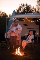 The family is relaxing together by the campfire near their mobile home. Evening family vacation photo
