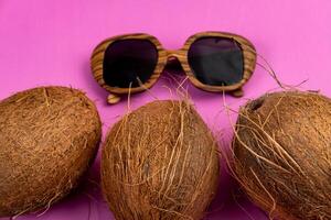 three whole coconuts and wooden glasses on a pink background photo