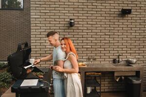 un casado Pareja cocineros A la parrilla carne juntos en su terraza foto