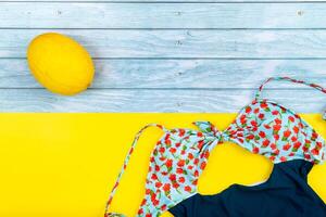 Top view of a swimsuit and a melon lying on a blue wooden and yellow background.Summer vacation concept photo