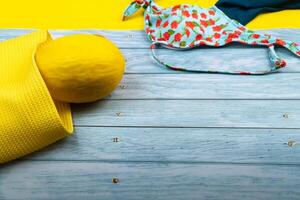 Top view of a swimsuit and a melon in a bag, lying on a blue wooden and yellow background.Summer vacation concept photo