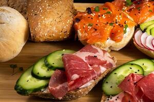 An assortment of sandwiches with fish, cheese, meat and vegetables lay on the board and a bun photo