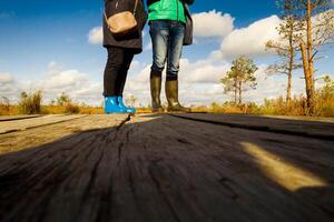 People in boots walk along a wooden path in a swamp in Yelnya, Belarus photo