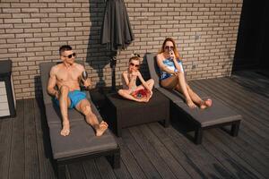 un contento familia en trajes de baño tomar el sol en verano en su terraza en Dom camas foto