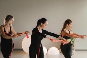 Girls in black are doing fitness with red ribbons indoors photo