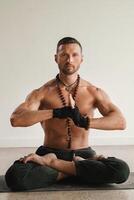 a man with a naked torso is sitting in the lotus position before doing yoga indoors. Fitness Trainer photo