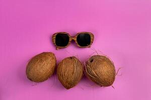 three whole coconuts and wooden glasses on a pink background photo