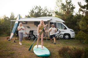 the family is resting next to their mobile home. My daughter is standing with a paddle on a sup board, and her parents pour water on her photo