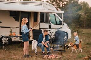 A family cooks sausages on a bonfire near their motorhome in the woods photo