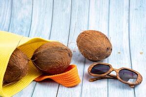 Whole coconuts lying in a yellow bag and glasses on a blue wooden background photo