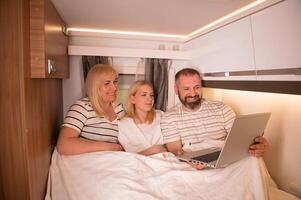 A family of three is watching a movie on a laptop while sitting in the bed of their motorhome photo