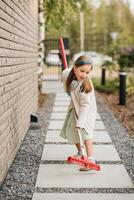 un pequeño niña con un cepillo limpia un camino en el calle en el patio foto