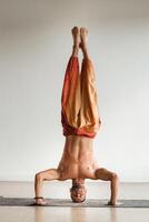 a man with a naked torso does yoga standing on his head indoors. Fitness Trainer photo