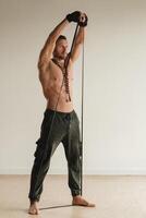 A man with a naked torso is engaged in strength fitness using a rubber loop indoors photo