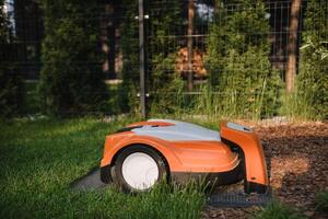 An orange robotic lawn mower stands on the base and is charged from electricity in the courtyard photo