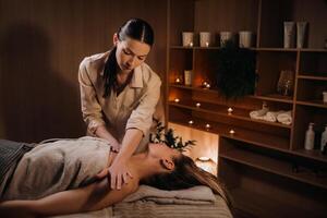 A masseuse gives a body massage to a woman in a spa center. A professional masseur massages the shoulder of a girl lying in a spa center photo