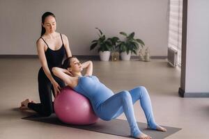 Pregnant woman with a trainer during fitness classes with a ball photo