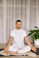 un hombre en blanco ropa de deporte es haciendo yoga con un aptitud habitación. el concepto de un sano estilo de vida foto