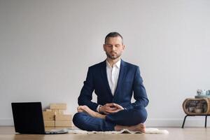 A man in a formal suit meditates while sitting in a fitness room with a laptop photo