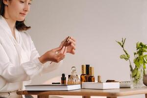 The aromatherapist girl is sitting in her office and holding a bottle of aromatic oils. there are essential oils on the table photo