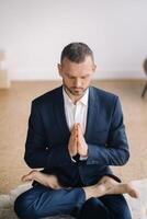 un hombre en un estricto traje lo hace yoga mientras sentado en un aptitud habitación foto