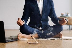 A man in a formal suit meditates while sitting in a fitness room with a laptop photo