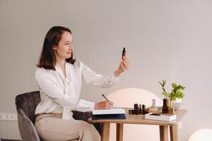 The aromatherapist girl is sitting in her office and holding a bottle of aromatic oil in her hands and writing something down. there are essential oils on the table photo