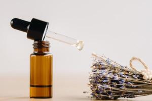 Essential oil in one bottle and dried lavender standing on the surface photo